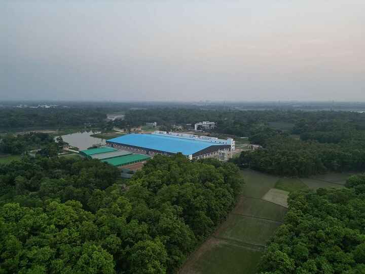 Drone shot of Karotoa Green factory complex with blue-roofed production unit set amid dense trees and open land.
